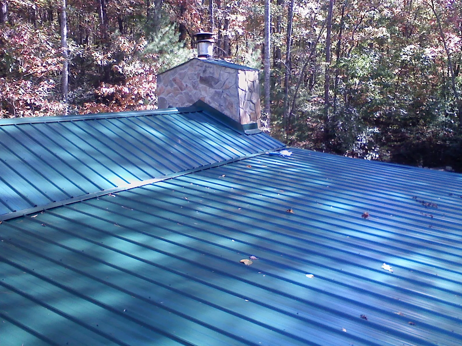 New green metal roof and stone chimney surrounded by autumn woods in Hilliard