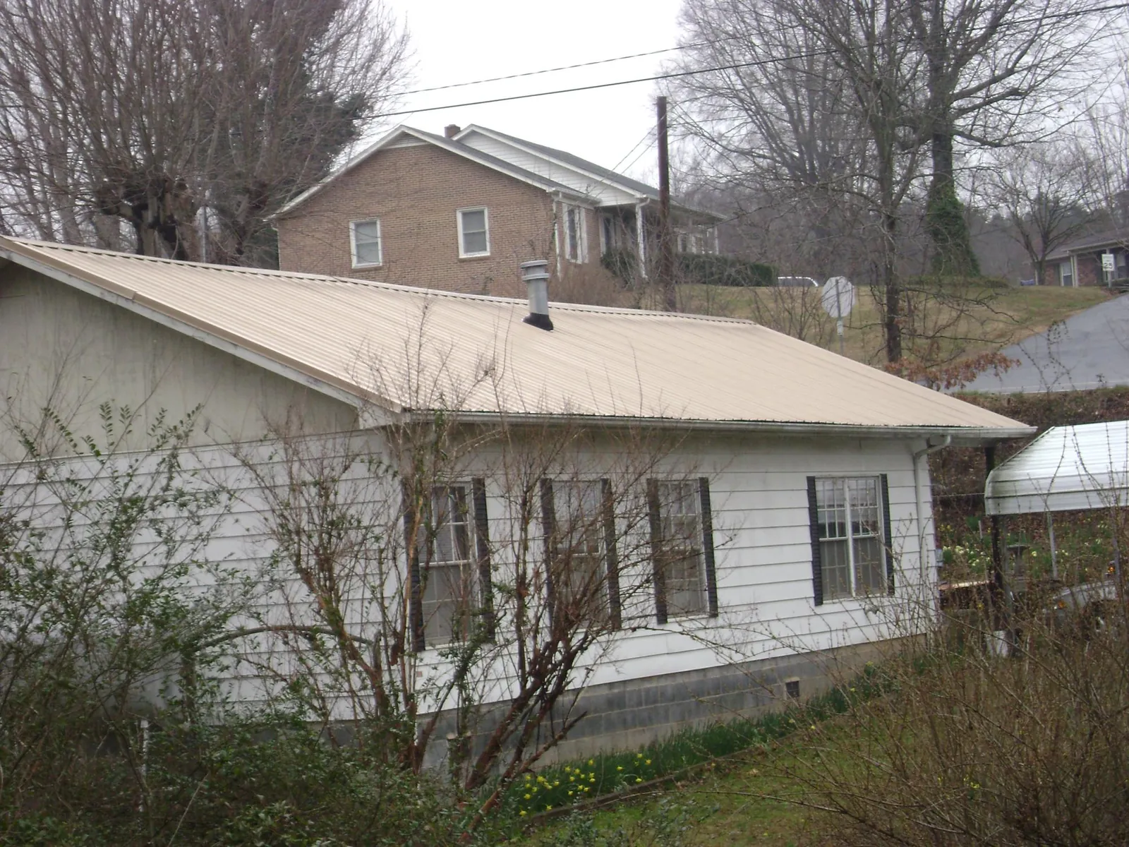 Tan metal roof on a white sided house set into a hillside — Commercial Roofing by Roofing Brothers in Hilliard